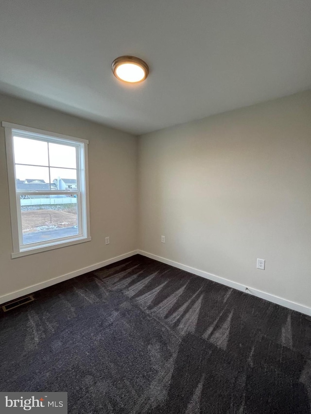 empty room featuring baseboards, dark carpet, and visible vents