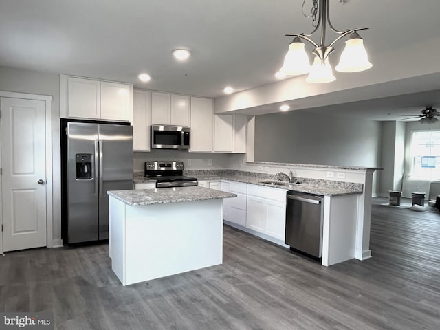 kitchen with a center island, appliances with stainless steel finishes, white cabinets, a sink, and decorative light fixtures