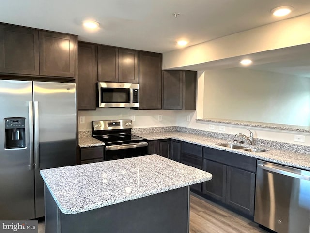 kitchen with a sink, light stone counters, appliances with stainless steel finishes, and light wood-style flooring