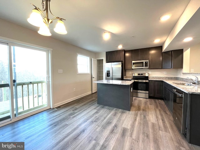 kitchen featuring stainless steel appliances, a sink, decorative light fixtures, light stone counters, and a kitchen island