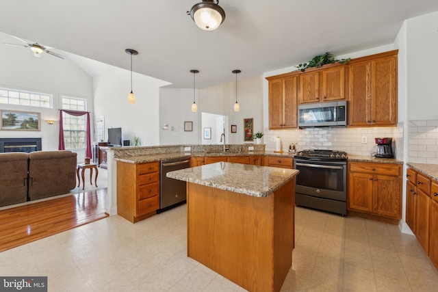 kitchen featuring a sink, open floor plan, hanging light fixtures, stainless steel appliances, and a peninsula