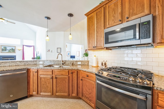 kitchen with a sink, light stone counters, pendant lighting, stainless steel appliances, and lofted ceiling