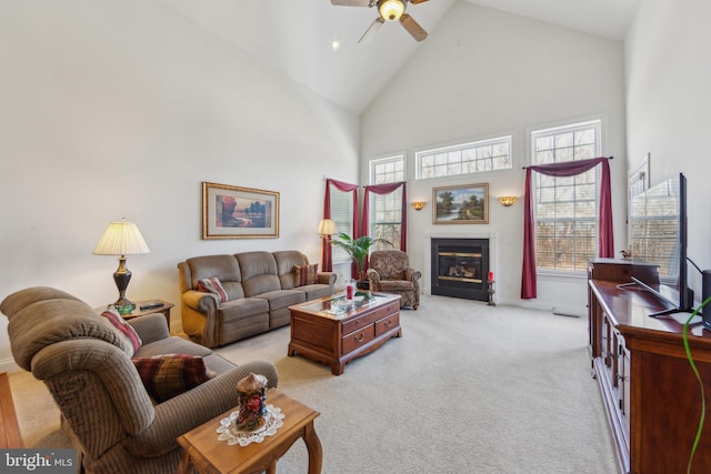 living room featuring high vaulted ceiling, light colored carpet, a ceiling fan, and a glass covered fireplace