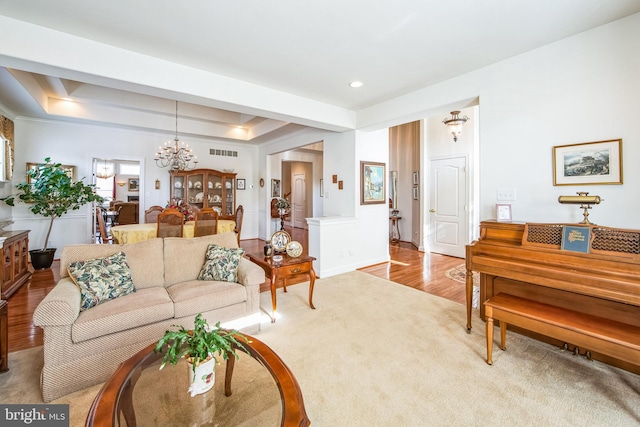 living room featuring an inviting chandelier, visible vents, a tray ceiling, light colored carpet, and light wood-style floors