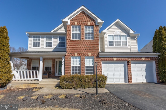 traditional home featuring a garage, a porch, brick siding, and aphalt driveway