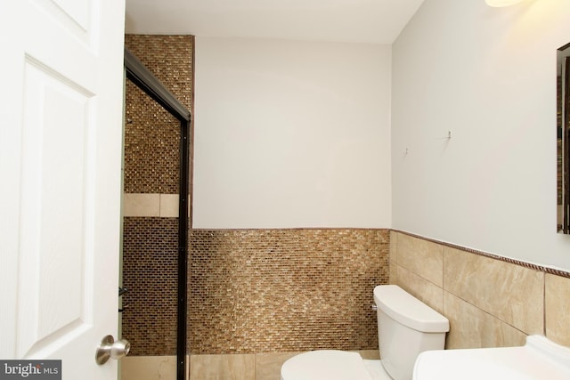 bathroom with toilet, a wainscoted wall, and tile walls