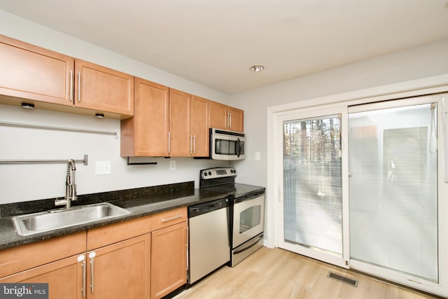 kitchen featuring stainless steel appliances, a sink, visible vents, light wood-type flooring, and dark stone countertops