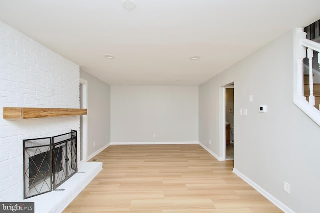 unfurnished living room with stairs, light wood finished floors, a brick fireplace, and baseboards