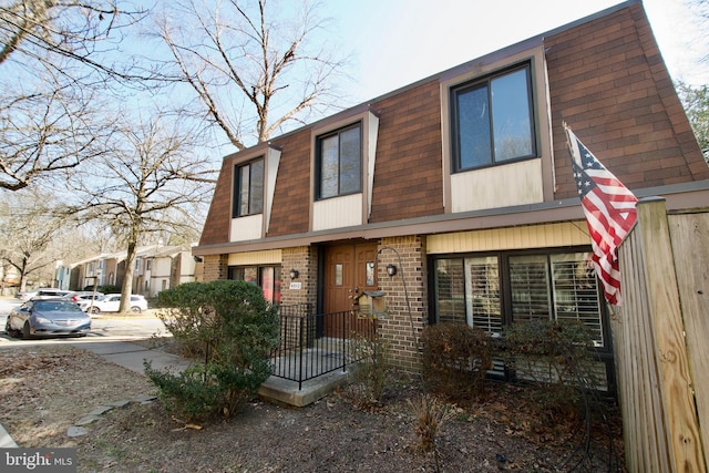 view of front of property featuring brick siding, mansard roof, and a shingled roof