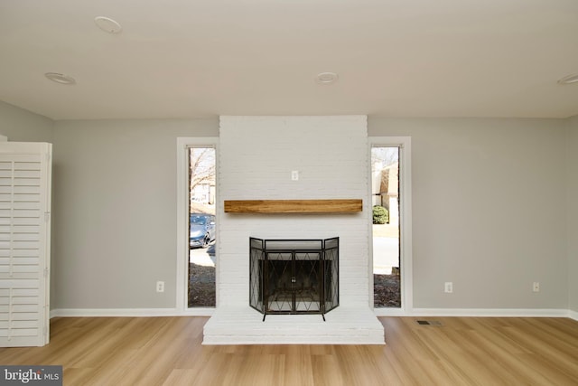 unfurnished living room featuring a brick fireplace, baseboards, visible vents, and light wood finished floors