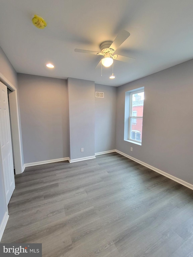 empty room with a ceiling fan, wood finished floors, visible vents, and baseboards