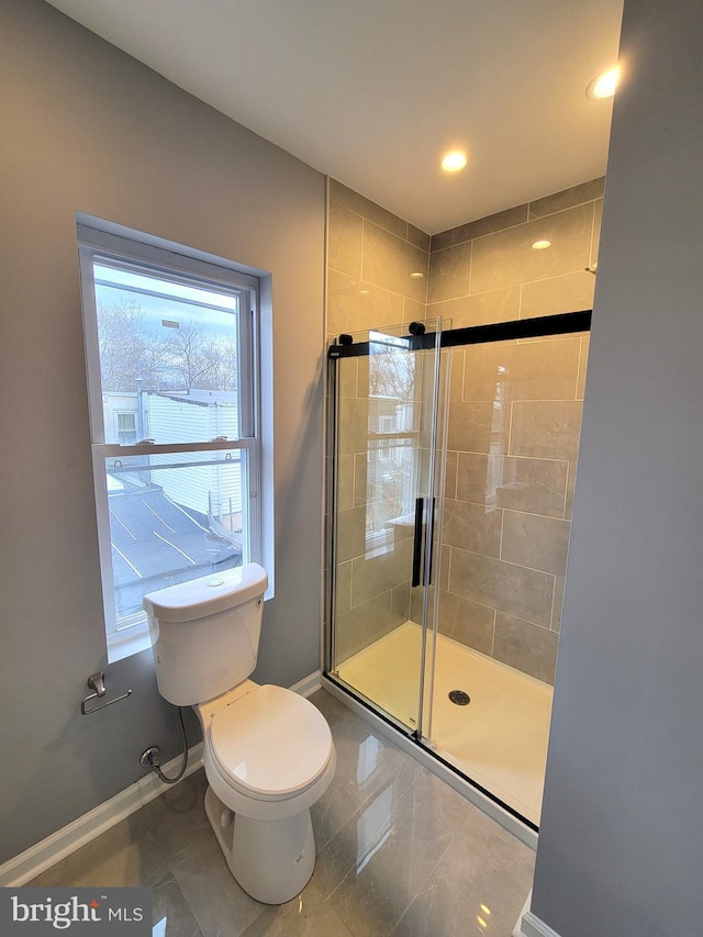 bathroom featuring toilet, a stall shower, and baseboards