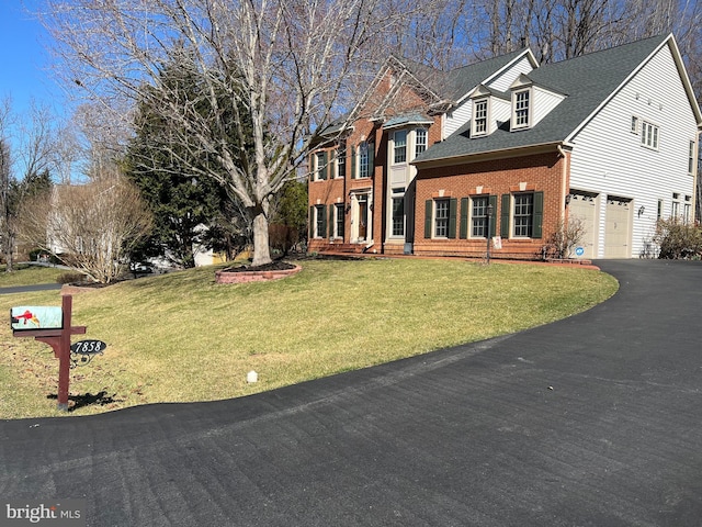 colonial-style house featuring roof with shingles, an attached garage, a front lawn, aphalt driveway, and brick siding