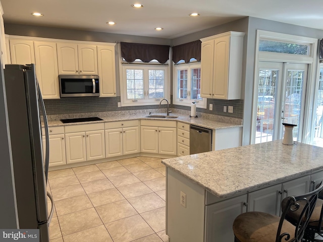 kitchen featuring a sink, backsplash, appliances with stainless steel finishes, light tile patterned floors, and light stone countertops