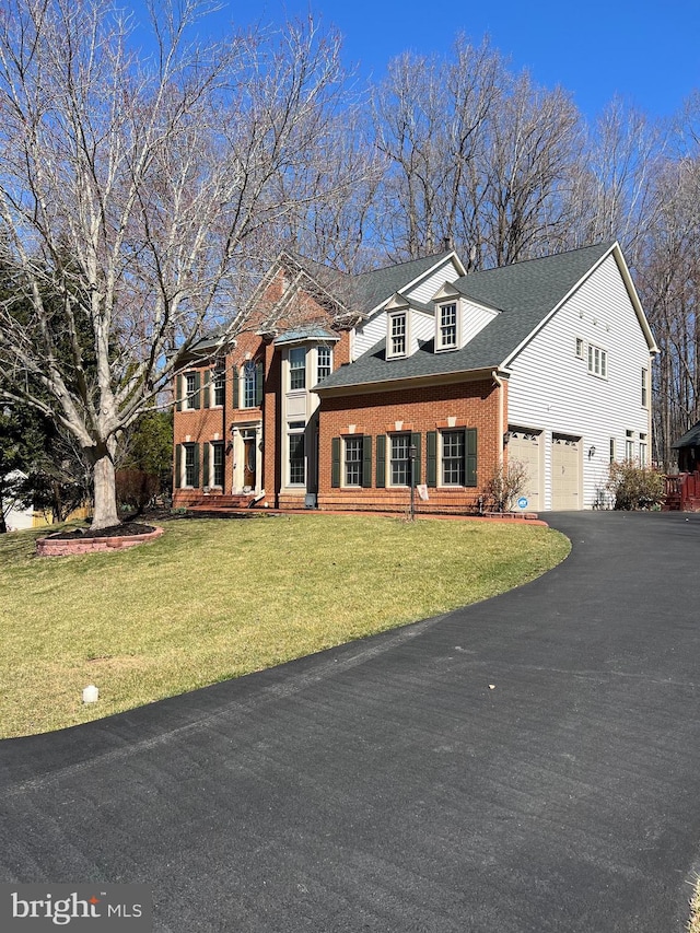 colonial house with brick siding, aphalt driveway, roof with shingles, a front yard, and a garage