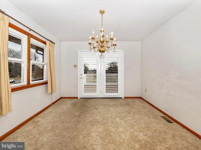 carpeted empty room featuring a chandelier, visible vents, and baseboards