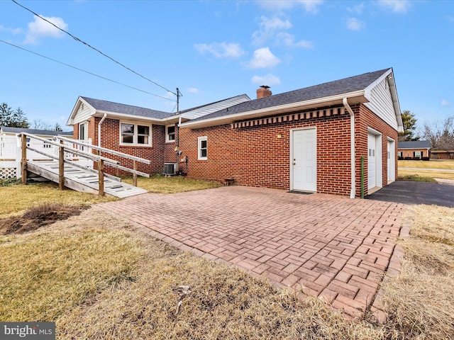 rear view of property featuring central AC unit, a garage, brick siding, decorative driveway, and a chimney