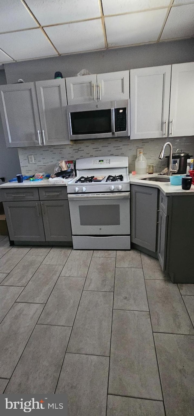 kitchen with gas range gas stove, light countertops, stainless steel microwave, decorative backsplash, and a sink