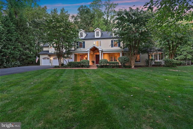 view of front of house with an attached garage, covered porch, aphalt driveway, and a front yard