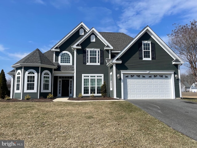 traditional-style home featuring a garage, driveway, a front yard, and roof with shingles