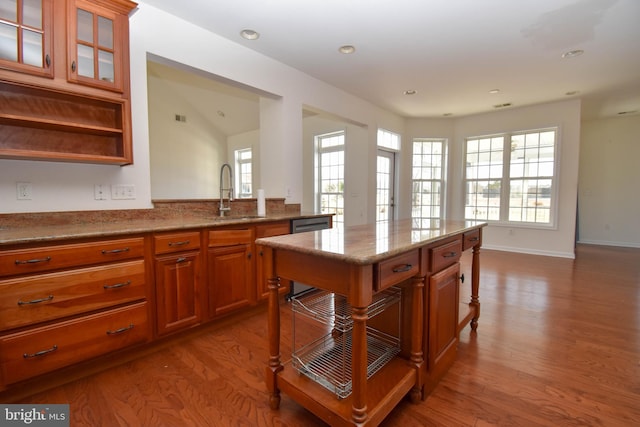 kitchen with brown cabinetry, a healthy amount of sunlight, wood finished floors, and a sink