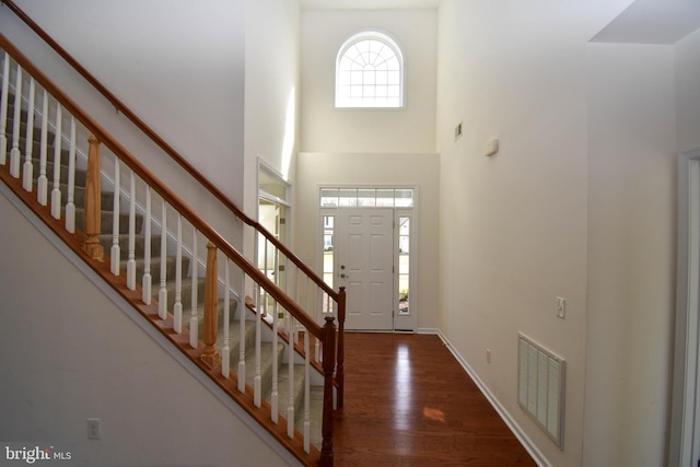 foyer with stairs, a high ceiling, wood finished floors, and visible vents