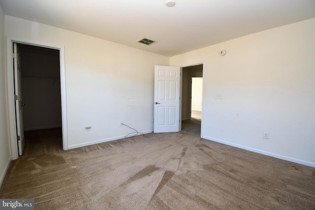 unfurnished bedroom with visible vents, a walk in closet, a closet, carpet flooring, and baseboards