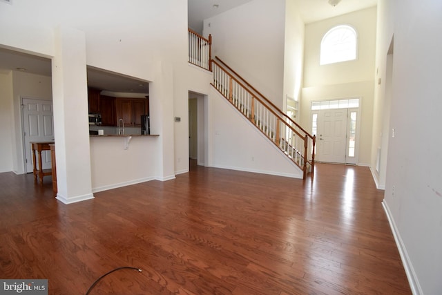 unfurnished living room with stairs, a high ceiling, dark wood-style floors, and baseboards