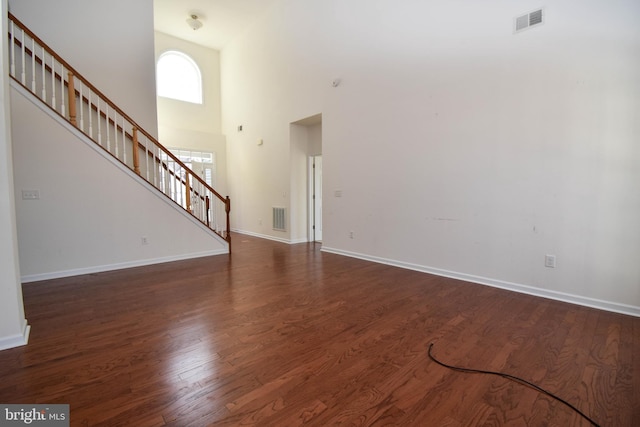 unfurnished living room with visible vents, baseboards, wood finished floors, and stairs