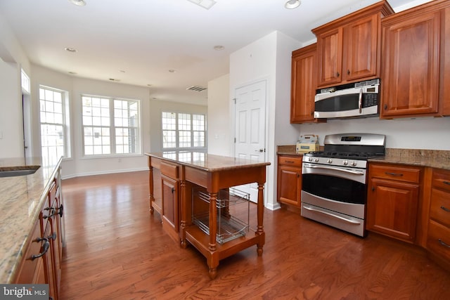 kitchen with brown cabinetry, visible vents, light stone countertops, dark wood finished floors, and stainless steel appliances