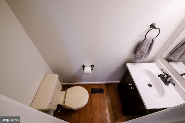 half bath with baseboards, visible vents, toilet, wood finished floors, and vanity