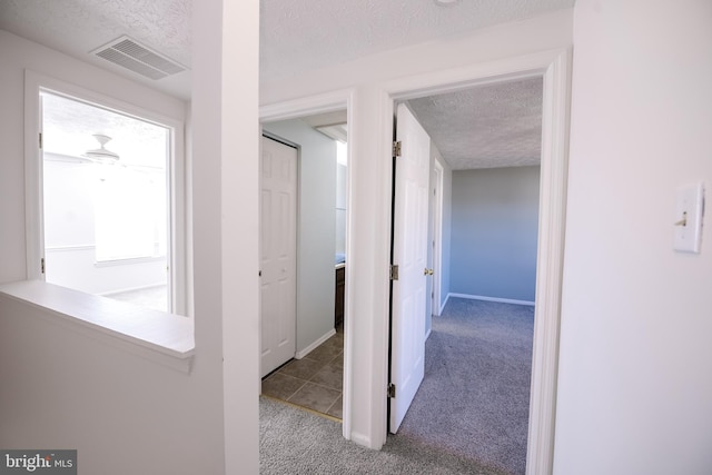 hallway with a textured ceiling, carpet, visible vents, and baseboards