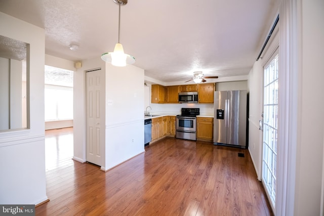 kitchen with brown cabinets, dark wood-style flooring, stainless steel appliances, light countertops, and a sink