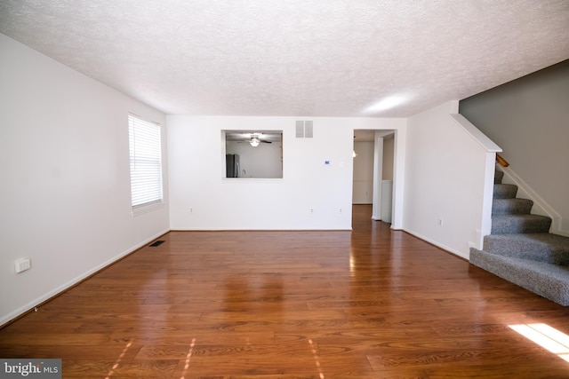 unfurnished living room featuring visible vents, ceiling fan, stairway, wood finished floors, and a textured ceiling