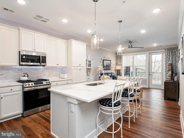 kitchen featuring appliances with stainless steel finishes, a kitchen island with sink, a sink, and white cabinetry