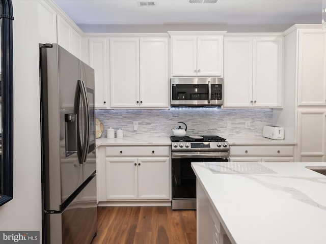 kitchen with dark wood-style floors, appliances with stainless steel finishes, white cabinets, and decorative backsplash