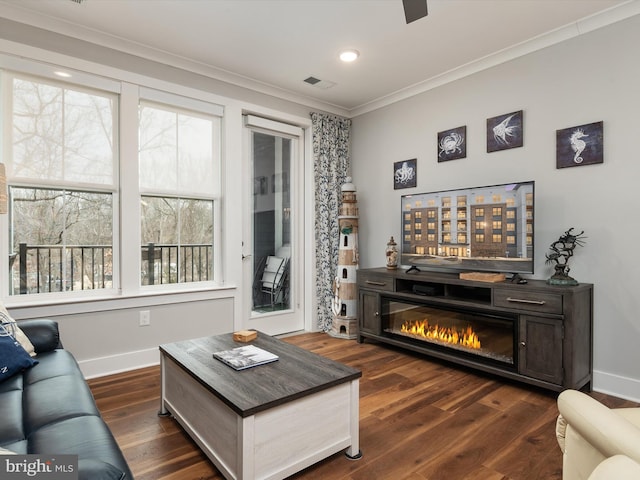 living room with baseboards, visible vents, a glass covered fireplace, ornamental molding, and dark wood-style flooring