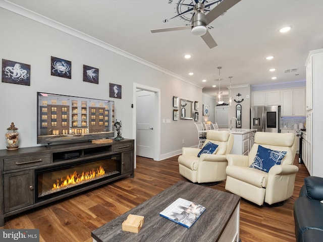 living area with ornamental molding, dark wood finished floors, a glass covered fireplace, and recessed lighting