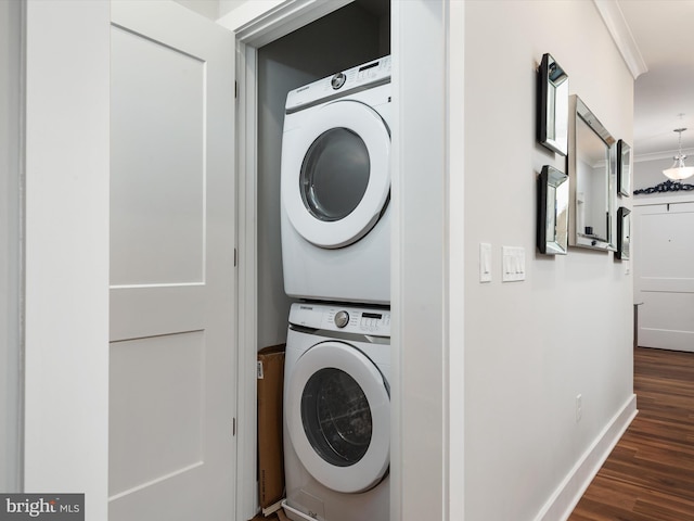 clothes washing area featuring dark wood-style floors, crown molding, stacked washer and dryer, laundry area, and baseboards