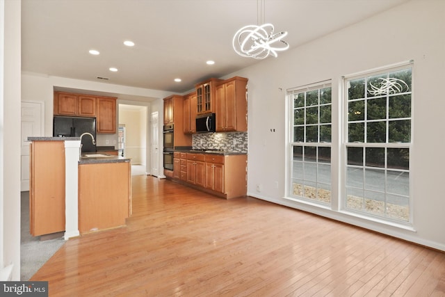 kitchen with brown cabinets, dark countertops, hanging light fixtures, glass insert cabinets, and black appliances