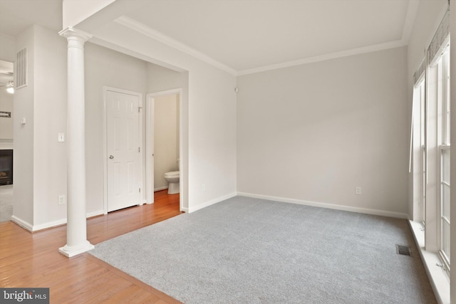 unfurnished bedroom featuring wood finished floors, visible vents, baseboards, ornamental molding, and decorative columns