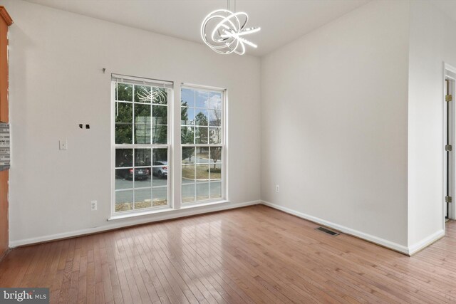 unfurnished dining area with light wood-type flooring, baseboards, visible vents, and a chandelier