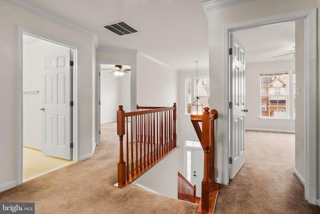 corridor with light colored carpet, visible vents, baseboards, an upstairs landing, and crown molding