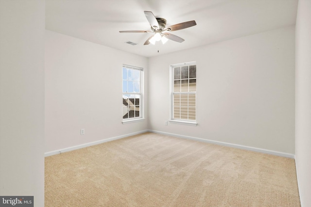 spare room with light carpet, ceiling fan, visible vents, and baseboards