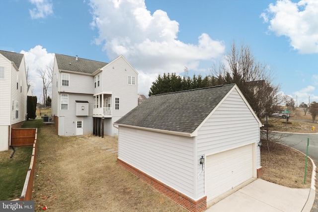 exterior space with roof with shingles, a yard, a detached garage, central AC unit, and a balcony