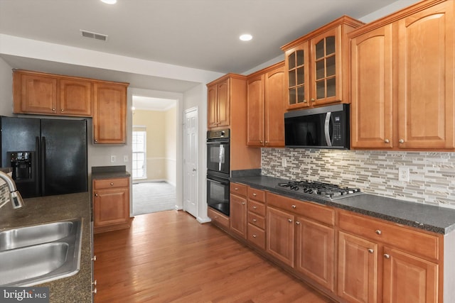 kitchen featuring a sink, visible vents, decorative backsplash, black appliances, and glass insert cabinets