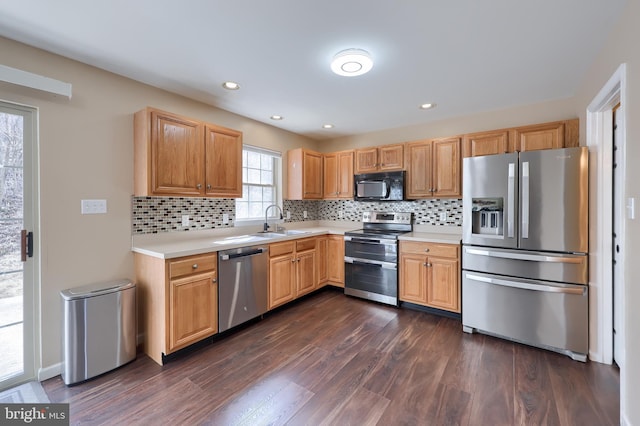 kitchen featuring a sink, light countertops, appliances with stainless steel finishes, decorative backsplash, and dark wood finished floors