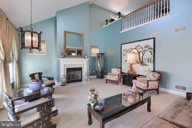 living room featuring high vaulted ceiling, a glass covered fireplace, visible vents, and light colored carpet