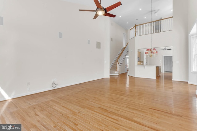 unfurnished living room with light wood-type flooring, baseboards, stairway, and ceiling fan with notable chandelier