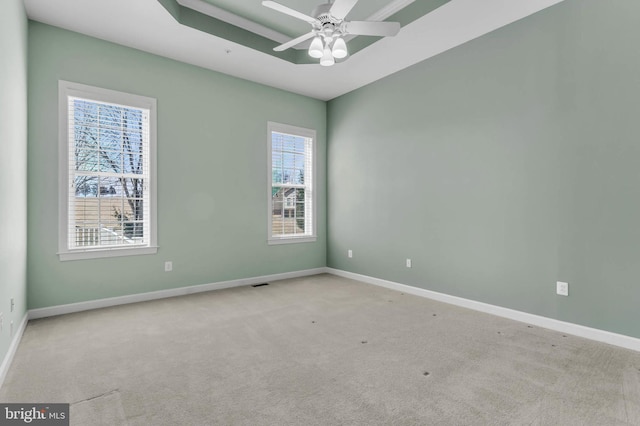 carpeted spare room with a raised ceiling, visible vents, baseboards, and ceiling fan